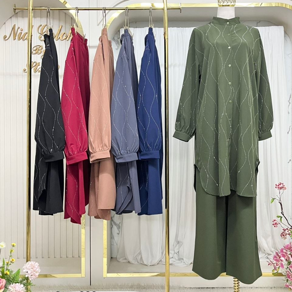 A clothing display in a boutique setting showing a green long-sleeve button-up tunic top with matching wide-leg pants on a mannequin, alongside several other color options hanging on a gold-framed rack. Indonesian text overlays show product details and pricing.
