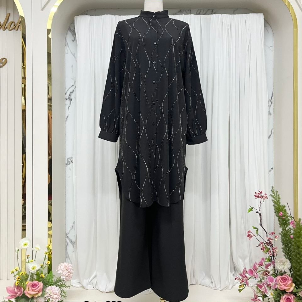 A black long kurta with white zigzag embroidered lines and black wide-leg pants displayed on a mannequin in a decorative boutique setting with white curtains and floral arrangements.