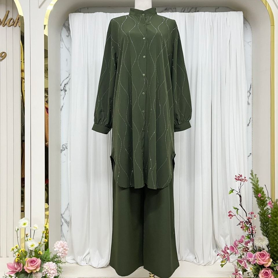 An olive green two-piece kurta set displayed on a mannequin in an elegant boutique setting. The set includes a long-sleeve button-up shirt with a subtle geometric pattern and matching wide-leg trousers.
